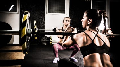 Two young women lifting weights on a cross training in the gym. They are preparing for snatch weightlifting. Young Caucasian women are both in their early thirties.