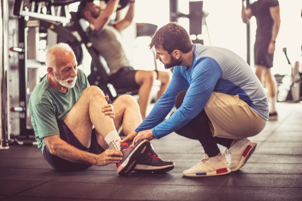 Personal trainer helping a senior male client who has sustained an injury during training.