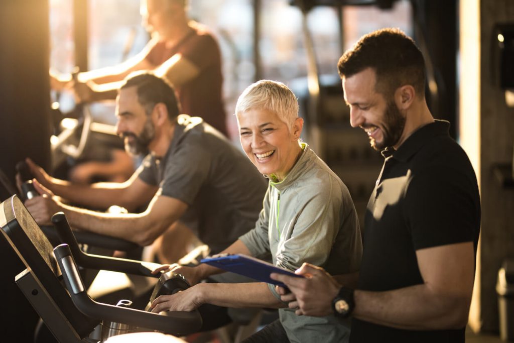 image of a male personal trainer training with two older clients on exercise bikes 