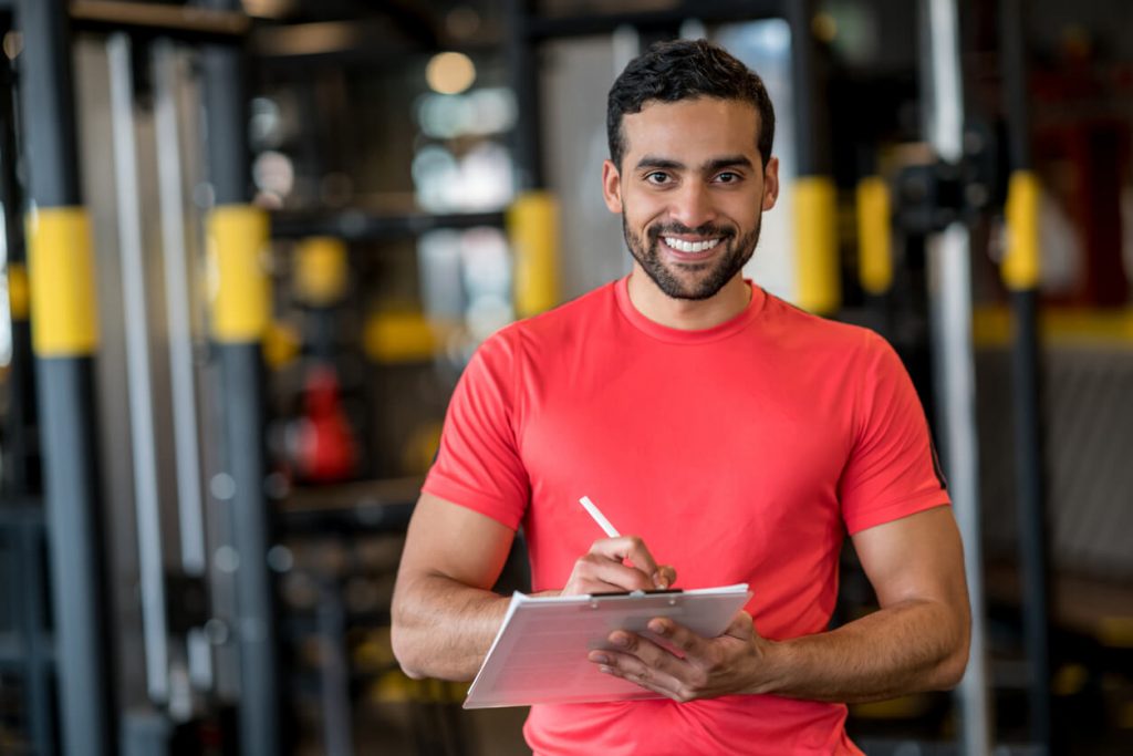 male fitness professional standing in a gym with a pen and clipboard 