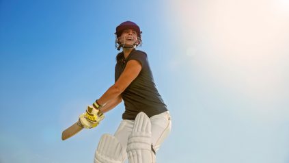 Women swinging cricket bat wearing cricket uniform playing on sunny day