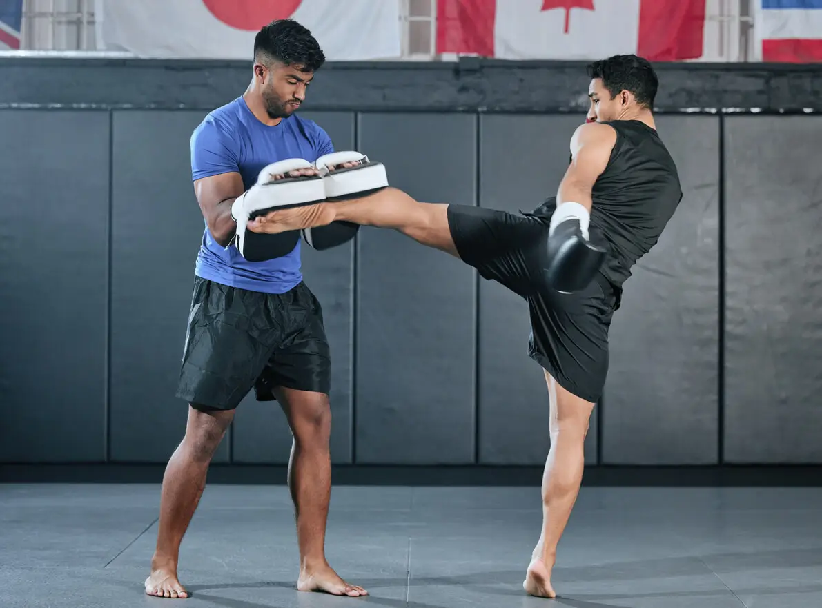 man practicing a MMA kick with their coach